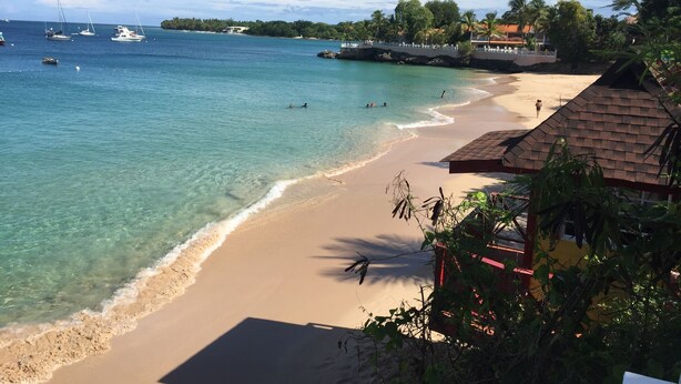 A beach with clear turquoise water, a sandy shore, and a few boats in the distance.