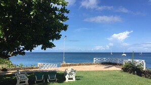 A grassy outdoor area with white chairs and a white fence overlooking the ocean.