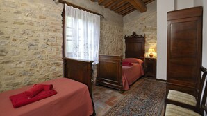 Une chambre avec deux lits, une armoire en bois, un mur en pierre et un tapis à motifs.