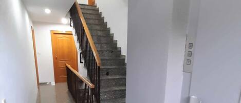 Een hal met een granieten vloer, een houten deur aan het einde en een trap met een houten leuning.