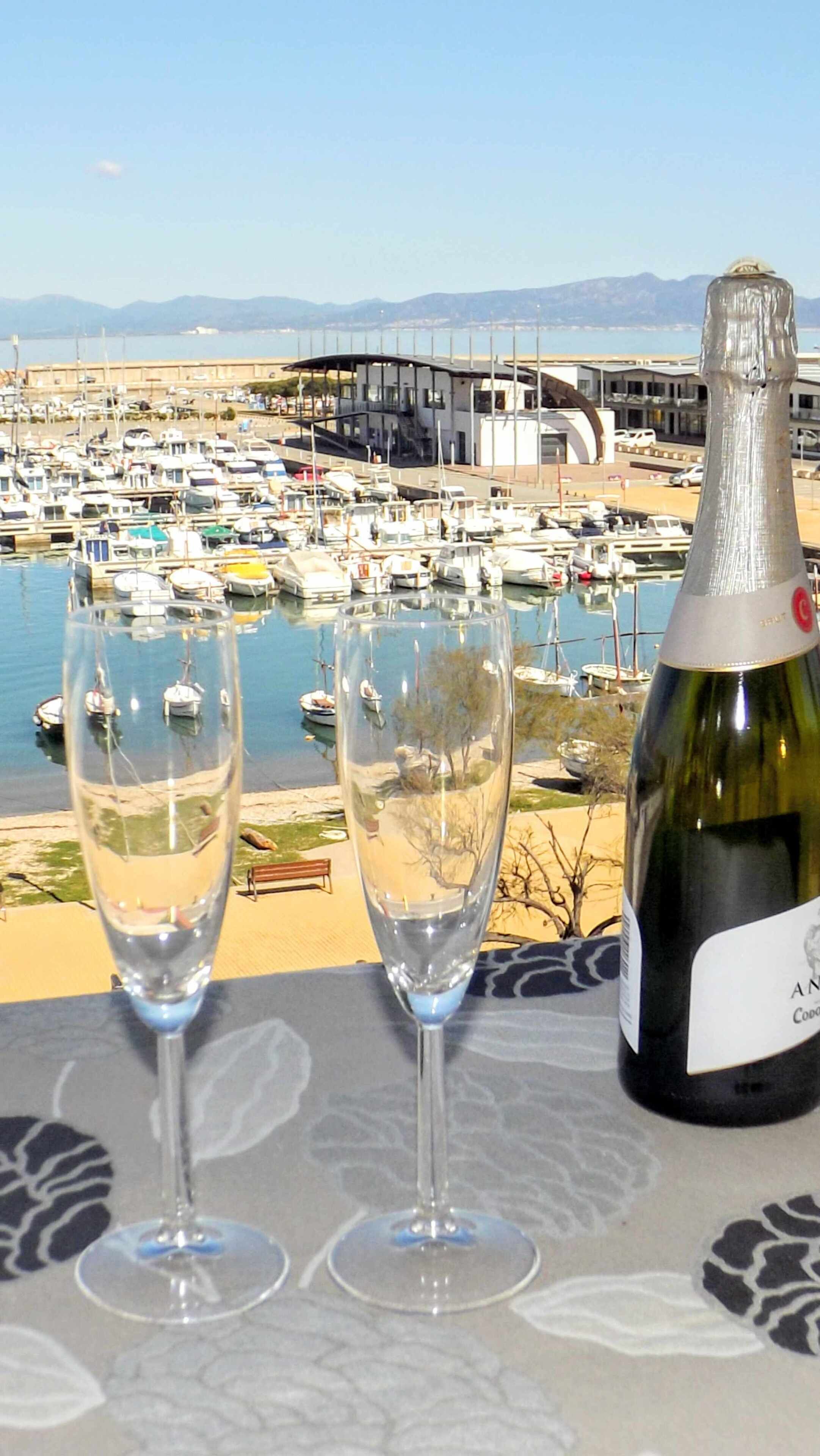Zwei leere Weingläser und eine Weinflasche auf einem Tisch mit Blick auf eine Marina und Boote.