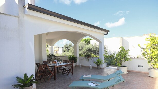 An outdoor patio with a table and chairs, two lounge chairs, and potted plants.