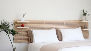 A bedroom with a wooden slat headboard, two white pillows, a beige throw blanket, and a potted plant.