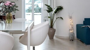 A modern living room with a white sofa, a dining table with chairs, a potted plant, and a blue couch.