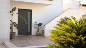 A modern building entrance with a dark door, potted plants, and a staircase leading to the upper level.