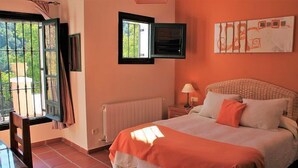 Un dormitorio con cama, ventana, radiador, lámpara y vistas a zonas verdes.