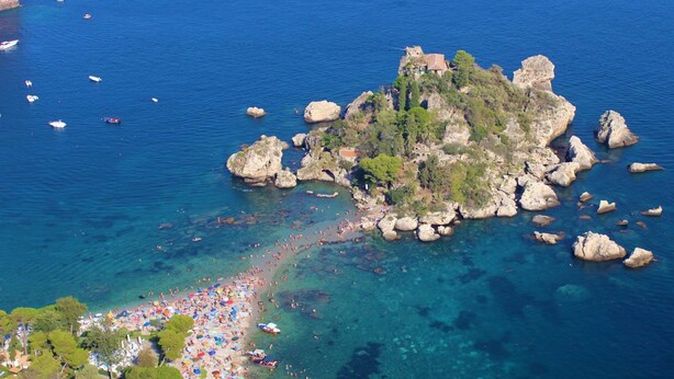 An aerial view of a coastal area with a beach, rocky outcrops, and boats.