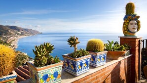 A terrace with potted cacti and succulents overlooking a coastal landscape.