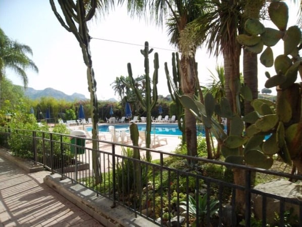 A pool area with lounge chairs and cacti, surrounded by a metal fence.