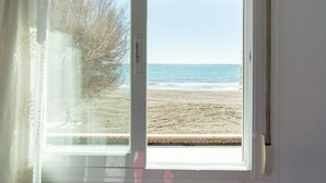 Ein Fenster mit Blick auf einen Strand, eine Steinmauer und einen Baum.