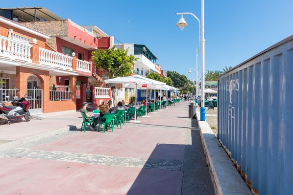 A street with outdoor seating, a row of green chairs, and a blue building with a sign.