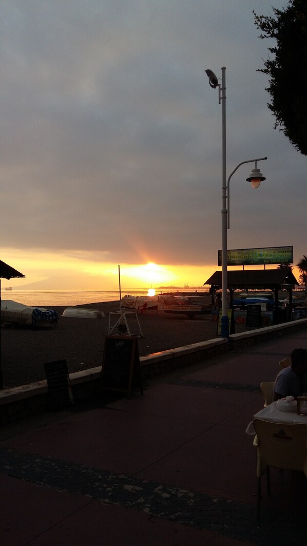 Blick auf einen Strand bei Sonnenuntergang, mit einer Straßenlaterne und einem Schild für 'STAURANTE ANTONIO'.