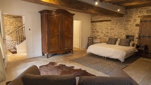 A bedroom with a stone wall, a wooden wardrobe, a bed with white bedding, and a leather sofa. - Newly renovated village home with views over the vines of Pommard (Pommard)