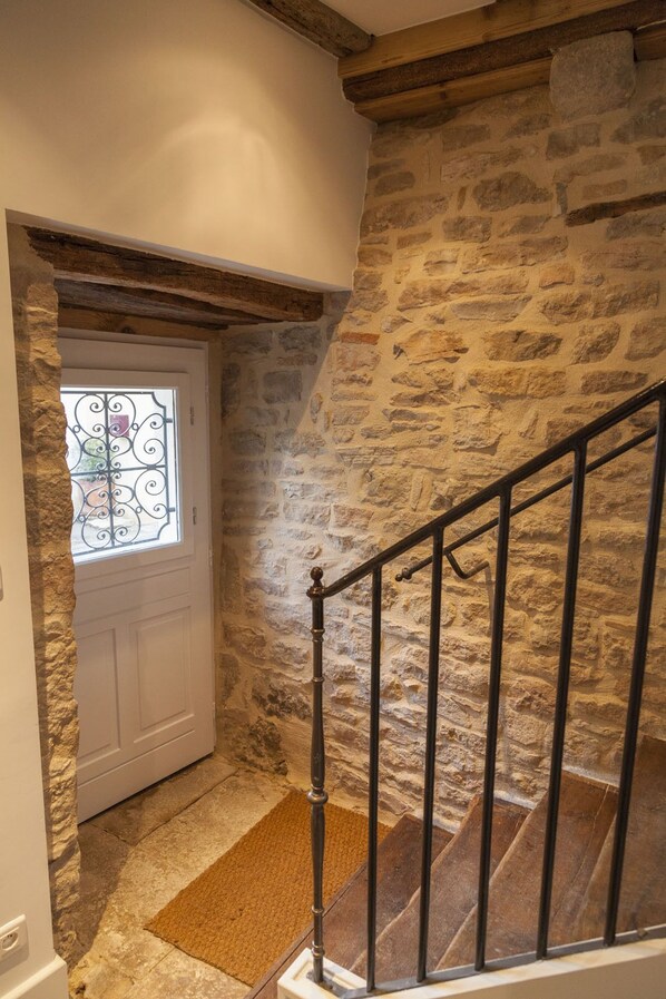 Una escala de pedra amb barana metàl·lica, una porta blanca amb un finestral de vidre decoratiu, i una paret de pedra.