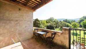 Een balkon met een tafel en stoelen, uitzicht op groen en heuvels, en een houten plafond.