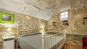 Slaapkamer met een stenen muur, een metalen bedframe, een nachtkastje met een lamp en een rode stoel.