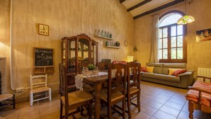 Een gezellige kamer met een houten eettafel, stoelen, een bank en een raam met uitzicht op groen.