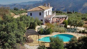 A two-story villa with a swimming pool, surrounded by lush greenery and mountains in the background. - Apartment with big terrace and fantastic views (Iznajar)