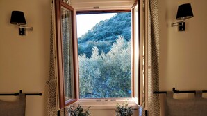 A room with a large window offering a view of a forested hillside. There are two wall-mounted lamps, a small table with a candle and two vases, and patterned pillows on a couch. - Apartment with big terrace and fantastic views (Iznajar)