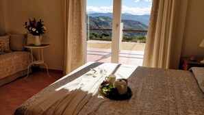 A hotel room with a bed, a small table with a vase of flowers, and a view of mountains through a glass door. - Apartment with big terrace and fantastic views (Iznajar)