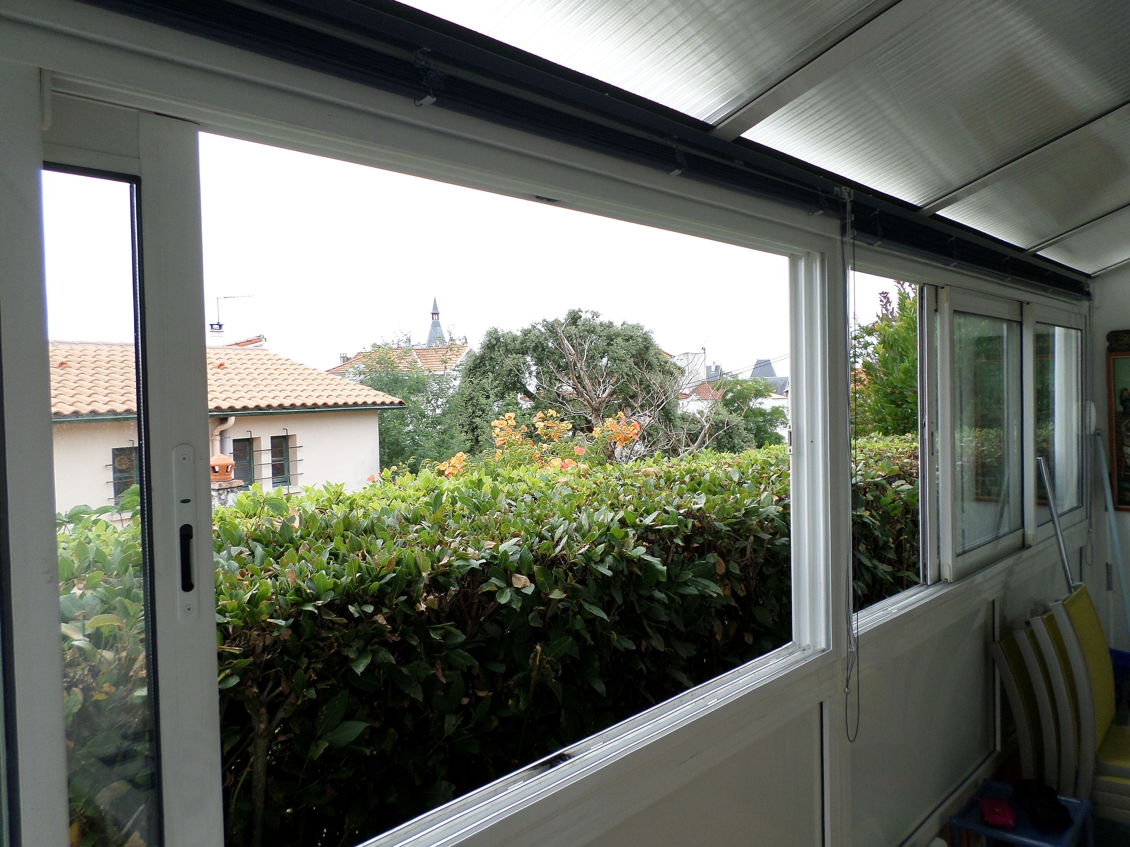 Une pièce dotée d’une grande fenêtre donnant sur un jardin et sur un bâtiment dont le toit est recouvert de tuiles.