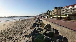 Une promenade en bord de mer, avec une barrière rocheuse, une plage et une rangée d’immeubles à plusieurs étages dotés de balcons.