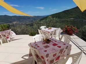 A terrace with white plastic chairs and tables, a potted plant, and a view of a mountainous landscape. - DINOABBO FARMHOUSE APP. OLEANDER CITR:008033-AGR.0001 CIN IT008033B5JCTY5SHI  (Lucinasco)