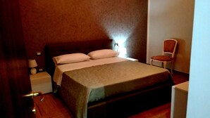 Un dormitorio con cama, mesitas de noche, una silla y un enchufe.