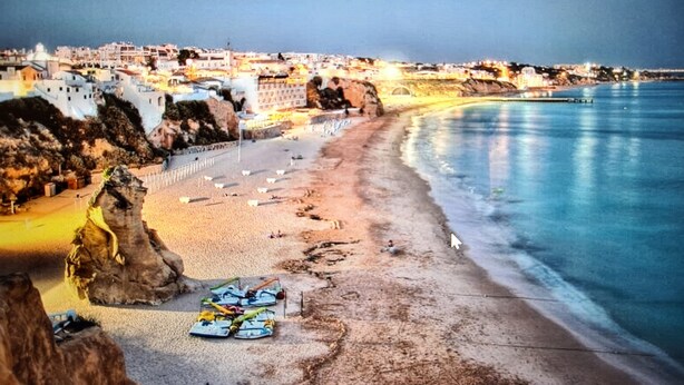 A coastal beach with a rocky outcrop, a sandy shore, and a row of beach umbrellas.