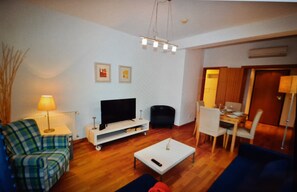 Sala de estar com sofá, mesa de centro, televisão e canto de jantar com cadeiras e mesa.