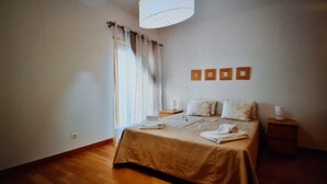 A bedroom with a bed, bedside tables, a hanging light fixture, and a window with curtains.