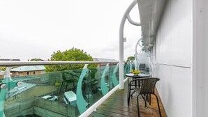 Ein Balkon mit Glasgeländer, der auf einen Parkplatz und ein Gebäude blickt.