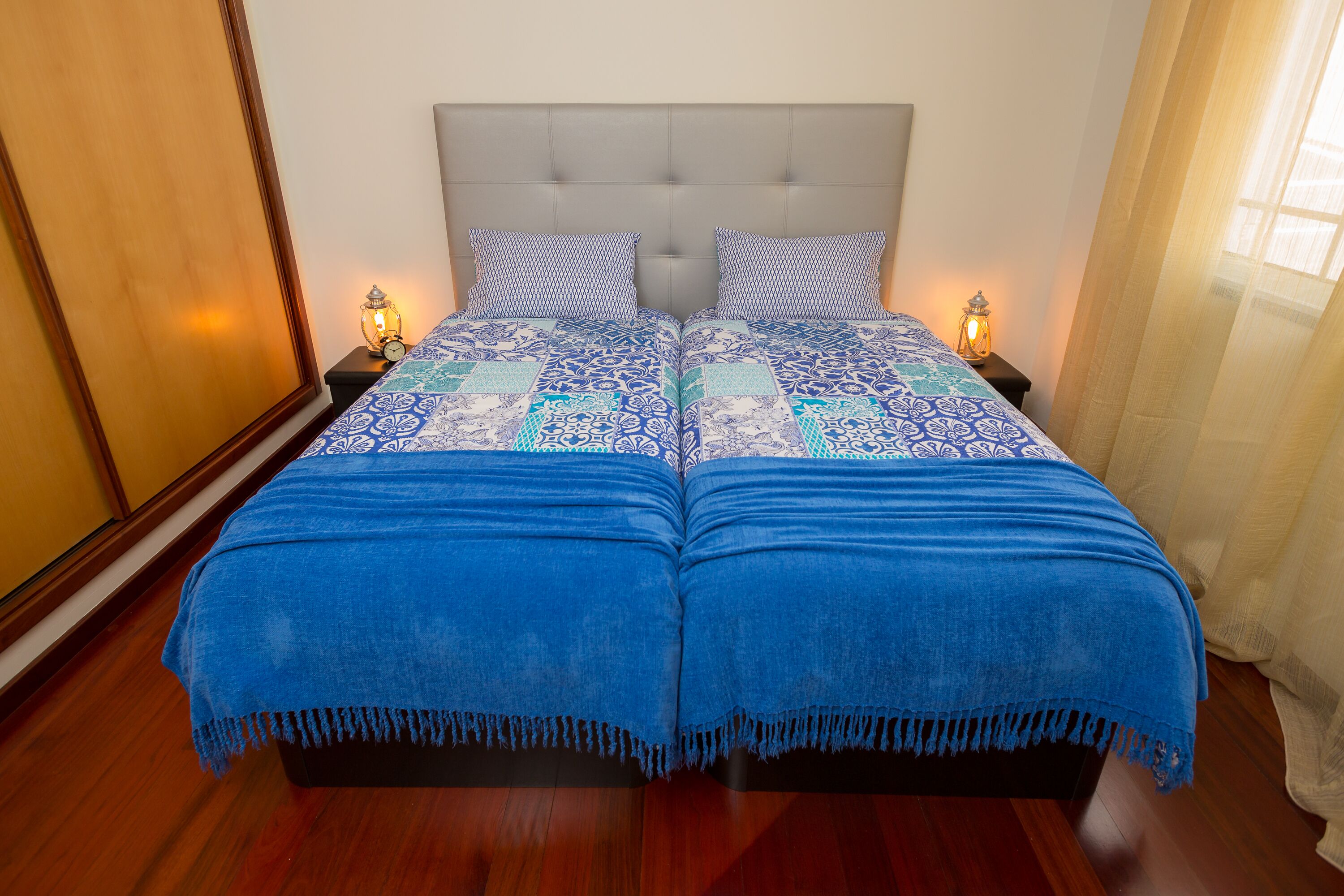 A double bed with a grey upholstered headboard, two bedside tables with lamps, and a blue blanket.