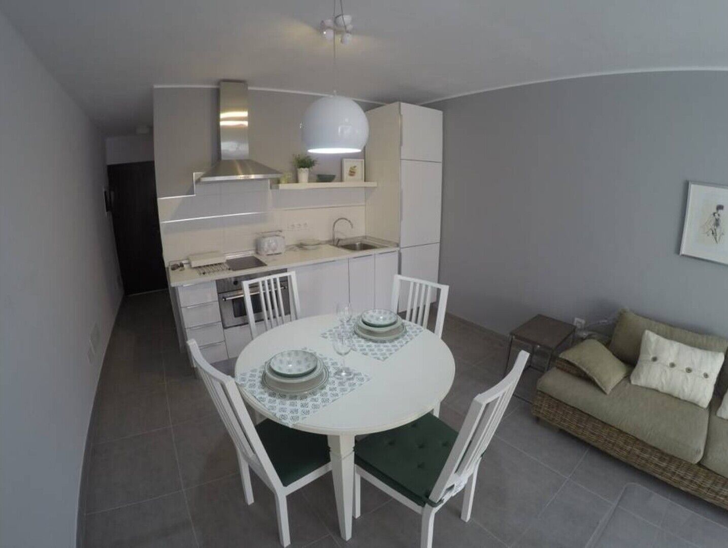 Une cuisine compacte avec un coin repas, des meubles blancs et un petit espace salon avec un canapé.