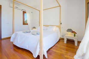 Quarto com cama de dossel, mesa de cabeceira com abajur e flores, e janela com cortinas.