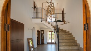 A grand staircase with a marble finish, leading to an upper floor. A large wooden door and a mirror are visible on the left. - Finca Ses Quaranta (Campos)