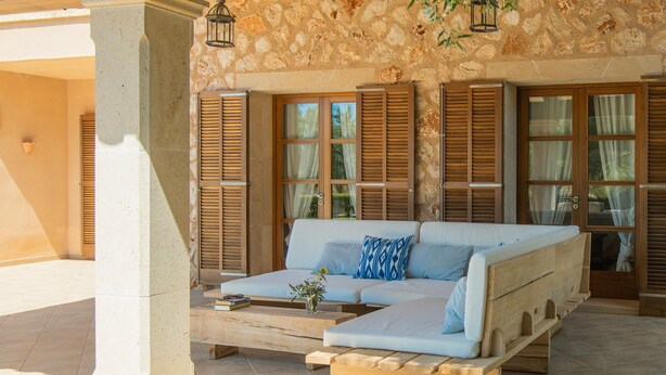 A cozy outdoor seating area with a wooden bench and a sofa, a stone wall, and wooden shutters. - Finca Ses Quaranta (Campos)