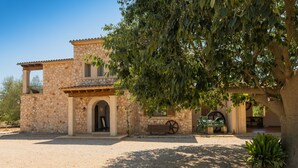 A stone building with a covered patio, a large tree in front, and a water wheel. - Finca Ses Quaranta (Campos)
