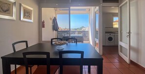 Ein Essbereich mit Tisch und Stühlen, eine kleine Küche mit Waschmaschine und Blick nach draußen.