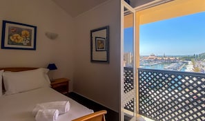 Une chambre d’hôtel avec un lit, deux tableaux encadrés, une table de chevet et un balcon donnant sur une marina.