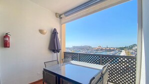 Un balcón con mesa y sillas, un extintor y vistas a un puerto deportivo con barcos y edificios.