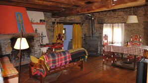 A rustic room with a stone fireplace, wooden beams, a checkered table, and a bench with colorful blankets. - Country house in Vall de Camprodon (Llanars)