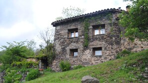 A stone building with a sloped roof, multiple windows, and surrounded by greenery. - Country house in Vall de Camprodon (Llanars)