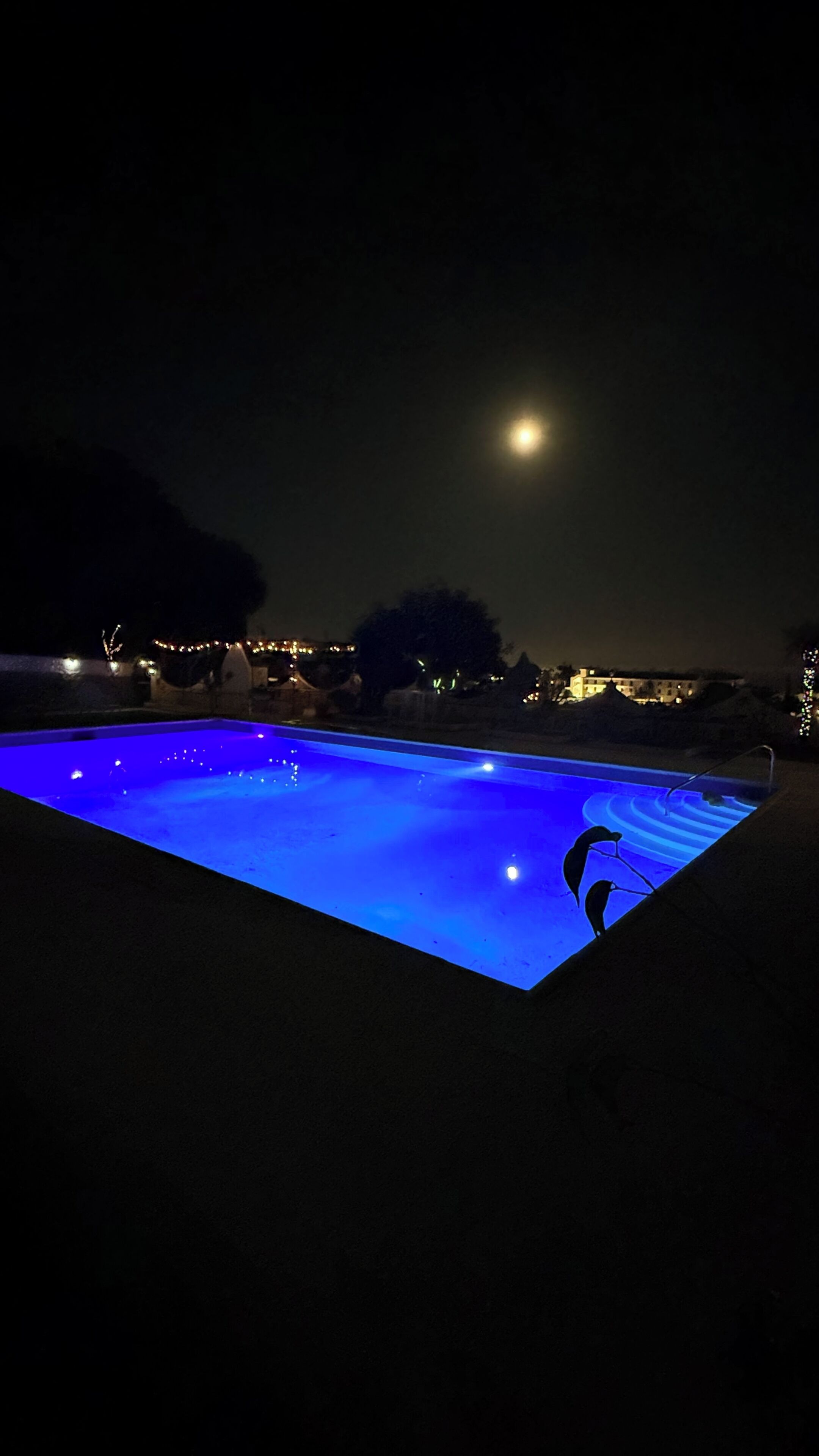 Una piscina por la noche con una luna visible en el cielo.
