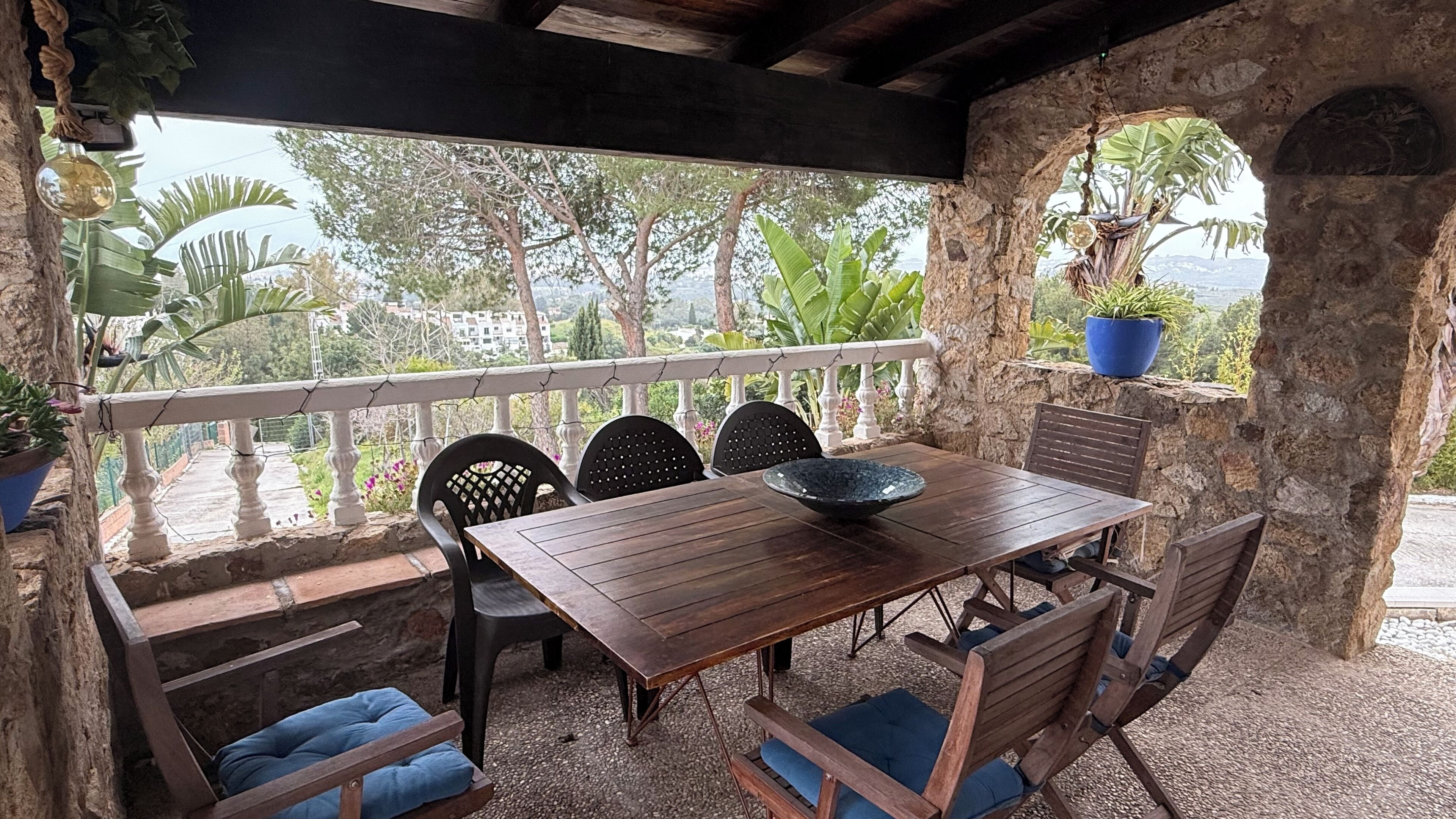 Eine Terrasse im Freien mit einem Holztisch und -stühlen, umgeben von Steinmauern und Blumentöpfen.