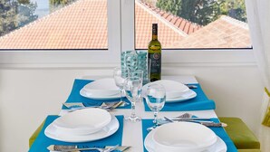 Mesa de jantar posta com pratos, talheres e uma garrafa de vinho, posicionada junto a uma janela com vista para uma paisagem montanhosa.