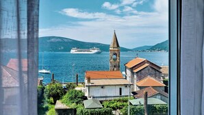 Uma vila costeira com uma torre de igreja imponente, um grande navio de cruzeiro ao fundo e vista clara do mar.