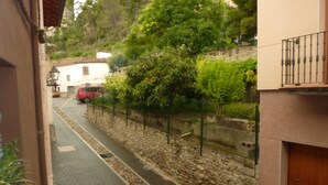 Una calle estrecha con pavimento de adoquines, una pared de piedra y una valla de metal.