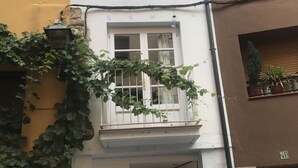 Un edificio de fachada blanca, con un balcón lleno de plantas y una puerta visible.