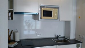 Eine kleine Küche mit weißen Schränken, einer Mikrowelle, einem Spülbecken und einer Deckenleuchte.